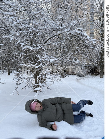 A woman lies happily in deep snow under a frosted tree, winter fun, playful outdoor lifestyle, frosty nature. A woman lies happily in deep snow under a frosted tree, winter fun, playful outdoor lifestyle, frosty nature. 136997695