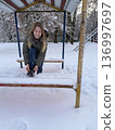A smiling woman sits on a snowy bench tying her boots during a winter walk, outdoor lifestyle, cold season activity, winter leisure. 136997697