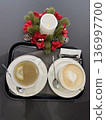 Top-down view of a black tray with lemon tea and a heart latte art cappuccino next to a festive candle, cozy cafe moment, winter holiday spirit, Christmas. 136997700