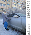 A woman opens the door of a frost-covered silver car on a snowy winter morning, daily commute, transportation routine, cold weather driving. 136997702