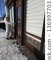 A woman in winter clothing opens the glass door to enter a building on a bright snowy day, urban lifestyle, daily errands, business entrance. 136997703