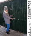 A woman in winter clothing enters a code on an electronic lock to open a green metal gate, outdoor security, residential access, winter lifestyle. 136997706
