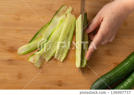 Slicing cucumbers with a large knife on wood cooking board close-up 136997737