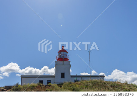 Farol da Ponta do Pargo lighthouse Madeira, white tower and red lantern on grassy headland 136998376