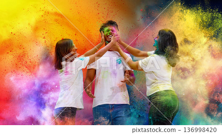 Two women playfully applying color on friend during Holi festival. Two women playfully applying color on friend during Holi festival. 136998420