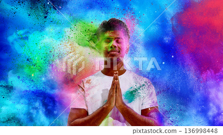 Young man praying during Holi festival with colorful powder explosion 136998448