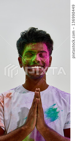 Smiling man with hands in namaste covered in colored powder. 136998449