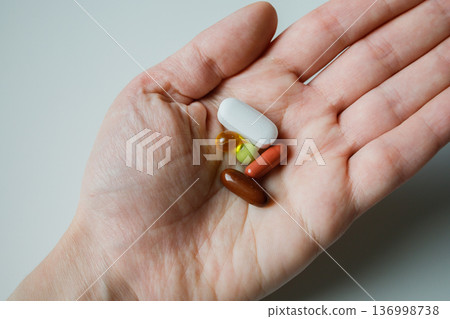 Different medical pills and capsules in woman hand close up. Medical pharmaceutical treatment at home. Daily dose of vitamins and supplements, biohacking. Different medical pills and capsules in woman hand close up. Medical pharmaceutical treatment at home. Daily dose of vitamins and supplements, biohacking. 136998738