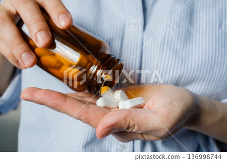 Woman pouring pills from small brown glass bottle to a hand. Taking medication at home, disease prevention, taking antidepressants, vitamins, dietary supplements. Healthcare and medicine. 136998744