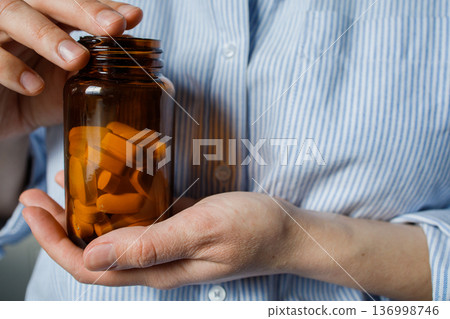 Brown glass bottle with pills in woman hands close up. Taking medication at home, disease prevention, taking antidepressants, vitamins, dietary supplements. Healthcare and medicine 136998746