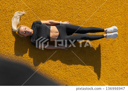 Athletic woman relaxing outdoors on vibrant surface with fitness attire Athletic woman relaxing outdoors on vibrant surface with fitness attire 136998947