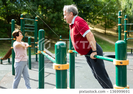 Senior man pulls up on crossbar in city park on sports ground Senior man pulls up on crossbar in city park on sports ground 136999691