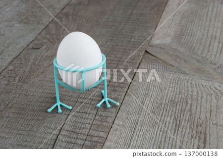 White chicken egg in blue funny stand on wooden background. Easter decor. 137000138