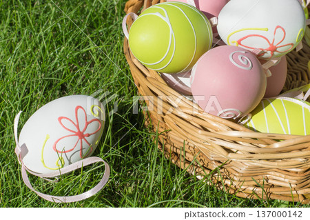 Easter painted pastel color eggs with ribbon in basket on green grass. 137000142