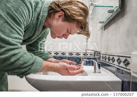 Young man washing face with water in bathroom sink Young man washing face with water in bathroom sink 137000207