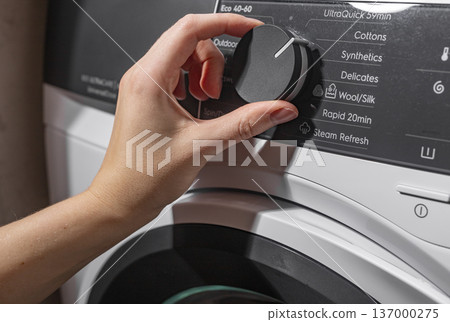 Hand selecting washing program on machine panel. Fingers turning control knob choosing cycle. Household appliance operation concept.. Hand selecting washing program on machine panel. Fingers turning control knob choosing cycle. Household appliance operation concept.. 137000275