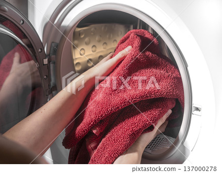 Hands inserting towels into dryer drum. Laundry placed inside drying machine appliance. Household care routine concept.. 137000278