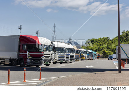 A row of large trucks parked in a line at a highway service area under a blue sky A row of large trucks parked in a line at a highway service area under a blue sky 137001595