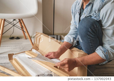 Man unboxing flat pack furniture and reading instructions Man unboxing flat pack furniture and reading instructions 137002043