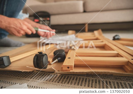 Man assembling wooden furniture using screwdriver at home Man assembling wooden furniture using screwdriver at home 137002050