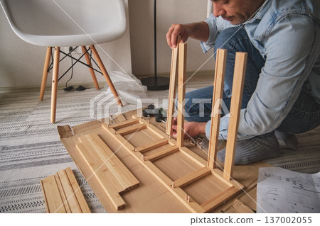 Man assembling furniture parts using screwdriver and instructions Man assembling furniture parts using screwdriver and instructions 137002055