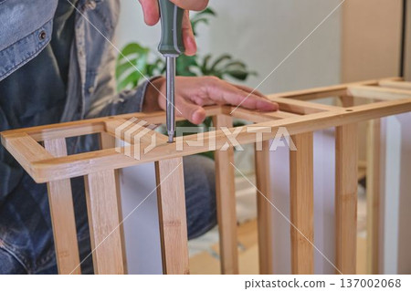 Person assembling wooden furniture with screwdriver at home Person assembling wooden furniture with screwdriver at home 137002068