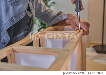 Person assembling wooden furniture with screwdriver at home Person assembling wooden furniture with screwdriver at home 137002071