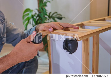 Handyman assembling furniture, attaching castor wheel to shelf 137002074