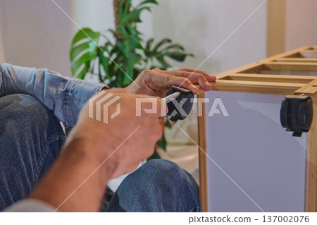 Person assembling furniture installing wheel casters with screwdriver Person assembling furniture installing wheel casters with screwdriver 137002076
