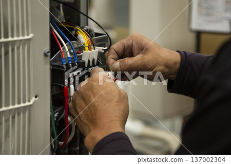 The hands of an electrician repairing the circuit board of an air conditioner outdoor unit The hands of an electrician repairing the circuit board of an air conditioner outdoor unit 137002304
