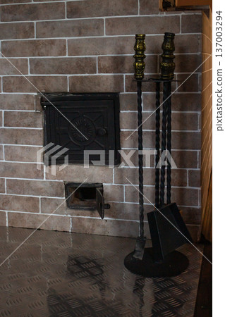 Traditional wood-burning fireplace. Beige brick construction with burning fire. Accessories stand. Cozy heating solution for home 137003294