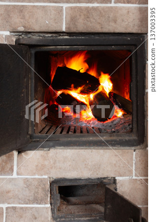 Brick fireplace with burning fire and open door. Fireplace tools on stand. Warm cozy home interior. Brick fireplace with burning fire and open door. Fireplace tools on stand. Warm cozy home interior. 137003395