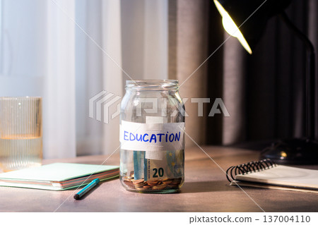 Savings jar for EDUCATION on table. Close up of money in transparent container representing financial planning and goal achievement Savings jar for EDUCATION on table. Close up of money in transparent container representing financial planning and goal achievement 137004110
