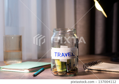 Savings jar for TRAVEL on table. Close up of money in transparent container representing financial planning and goal achievement Savings jar for TRAVEL on table. Close up of money in transparent container representing financial planning and goal achievement 137004112