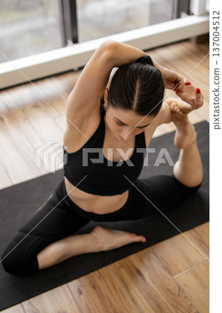 A woman in black athletic wear demonstrates a challenging yoga posture on a mat, showcasing flexibility and balance A woman in black athletic wear demonstrates a challenging yoga posture on a mat, showcasing flexibility and balance 137004512