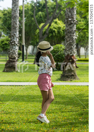 A young girl wearing a straw hat and a white shirt is standing in a grassy field A young girl wearing a straw hat and a white shirt is standing in a grassy field 137004555