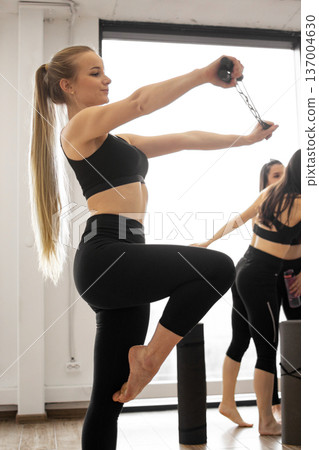 A fit woman in black activewear performs an exercise using a resistance band, focusing on her upper body strength and balance 137004630