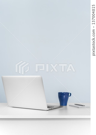 Laptop and coffee mug on white desk against blue wall 137004815