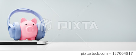 Piggy bank with headphones on laptop, podcast and fintech concept Piggy bank with headphones on laptop, podcast and fintech concept 137004817