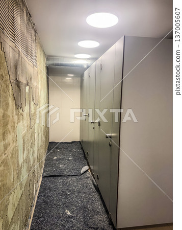 Locker room renovation in progress. New grey lockers next to an unfinished wall with exposed tile adhesive. 137005607