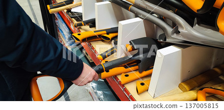 A person's hand selects one of the shovels on the store shelves. Concepts include home renovation, spring gardening preparation, construction work, DIY projects, and gardening. A person's hand selects one of the shovels on the store shelves. Concepts include home renovation, spring gardening preparation, construction work, DIY projects, and gardening. 137005815