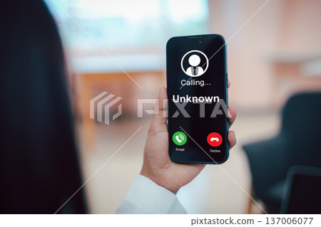 Close up of a hand holding a smartphone with an unknown incoming call screen. Concept of telephone scam, phishing attack, cyber fraud, identity theft, and mobile security awareness. Close up of a hand holding a smartphone with an unknown incoming call screen. Concept of telephone scam, phishing attack, cyber fraud, identity theft, and mobile security awareness. 137006077