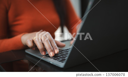 Close up of a woman's hands with orange nails typing on a laptop keyboard. Concept of remote work, professional freelancer, online business communication, and modern digital lifestyle. Close up of a woman's hands with orange nails typing on a laptop keyboard. Concept of remote work, professional freelancer, online business communication, and modern digital lifestyle. 137006078