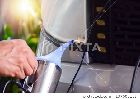 The technician is spraying a coating onto the car's headlights. The technician is spraying a coating onto the car's headlights. 137006115