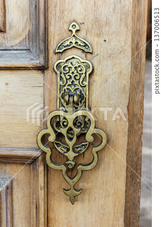 Ornate brass door knocker mounted on an aged door Ornate brass door knocker mounted on an aged door 137006513