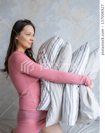 woman holds pile of pillows in her hands. pillows are in different colors, look like stack. woman holds pile of pillows in her hands. pillows are in different colors, look like stack. 137006927