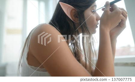 Caucasian woman applying detailed elf makeup near window Caucasian woman applying detailed elf makeup near window 137007775