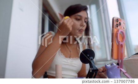Woman in mirror applying blush with pleasant expression and daylight 137007786