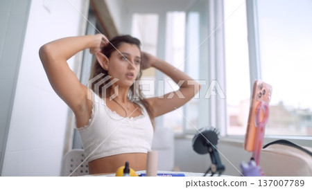 Young lady fixing her hair in sunlit modern studio for day Young lady fixing her hair in sunlit modern studio for day 137007789