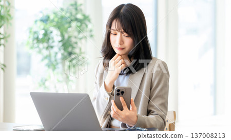 A woman/businesswoman thinking while looking at her smartphone 137008213